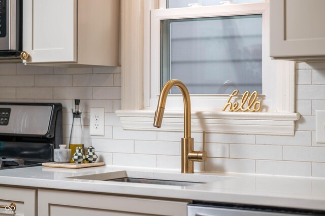 kitchen with appliances with stainless steel finishes, backsplash, a sink, and white cabinetry