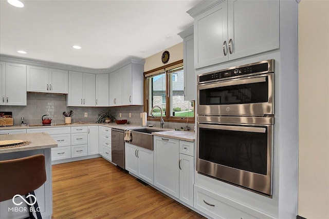 kitchen featuring a sink, light wood-style flooring, stainless steel appliances, recessed lighting, and decorative backsplash