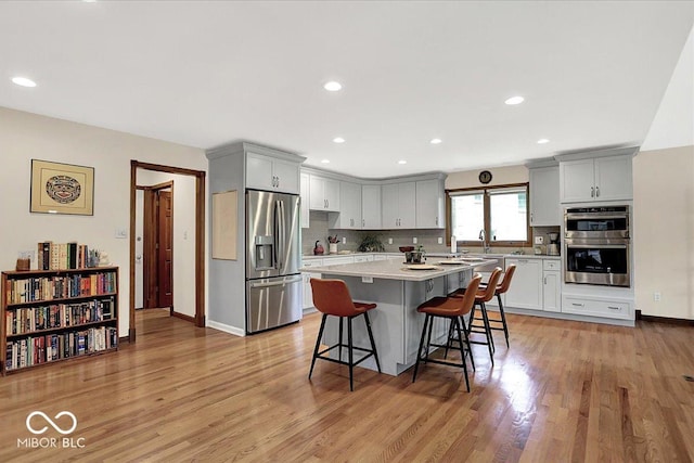 kitchen featuring a kitchen breakfast bar, appliances with stainless steel finishes, light wood finished floors, and tasteful backsplash