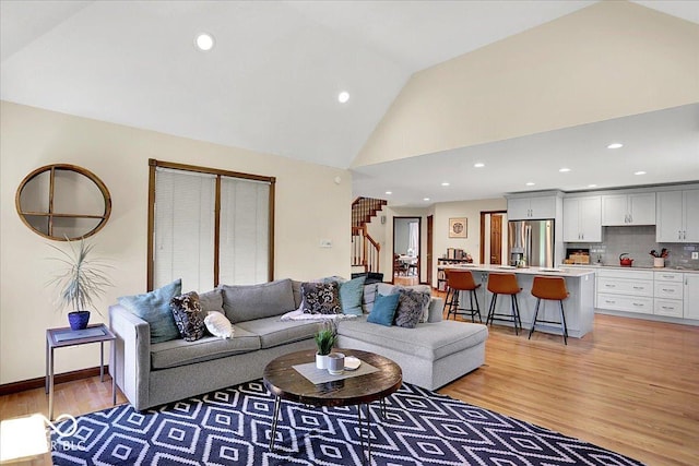 living room featuring light wood-type flooring, recessed lighting, high vaulted ceiling, and stairway