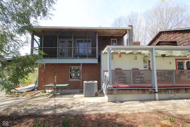 rear view of house featuring a sunroom, a patio area, brick siding, and central AC