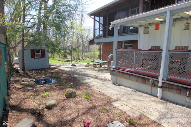 view of side of home featuring a storage shed, brick siding, a patio, an outbuilding, and a sunroom
