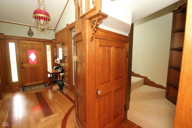 entrance foyer with vaulted ceiling, stairs, wood-type flooring, and a notable chandelier