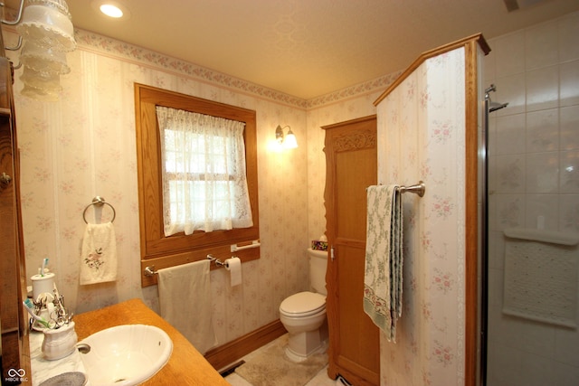 bathroom with toilet, tiled shower, vanity, and wallpapered walls
