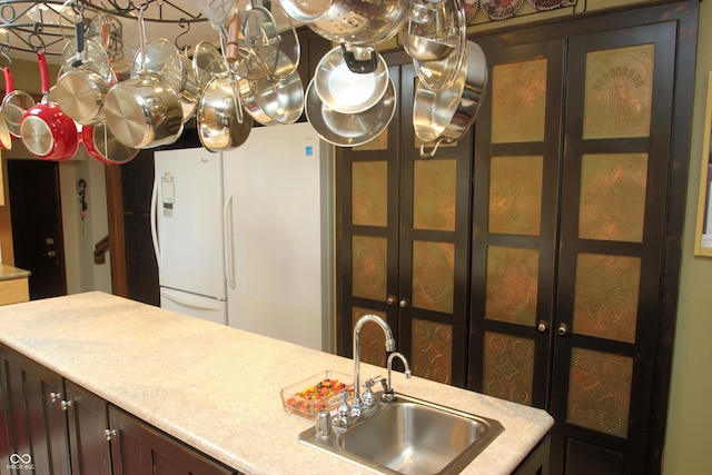 kitchen with light countertops, glass insert cabinets, dark brown cabinetry, and a sink