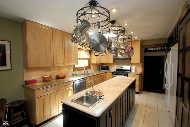 kitchen with light brown cabinets, a sink, a center island with sink, stainless steel appliances, and tasteful backsplash