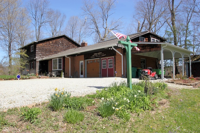 view of front facade featuring brick siding, a chimney, and gravel driveway