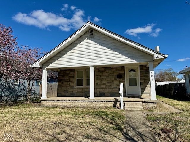 back of property with a lawn, fence, stone siding, and covered porch