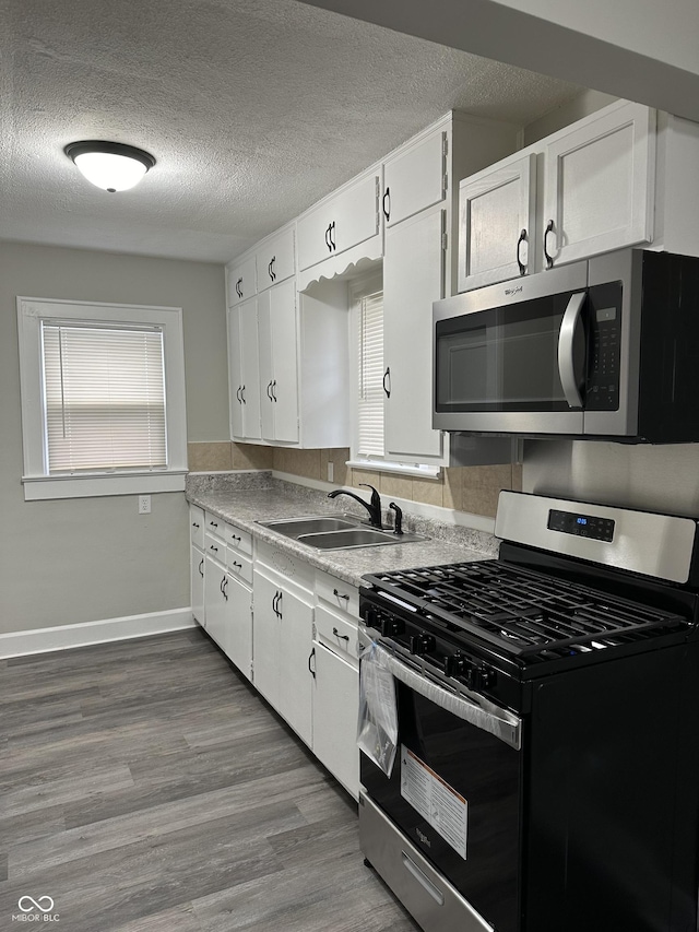 kitchen featuring wood finished floors, a sink, a textured ceiling, white cabinets, and appliances with stainless steel finishes