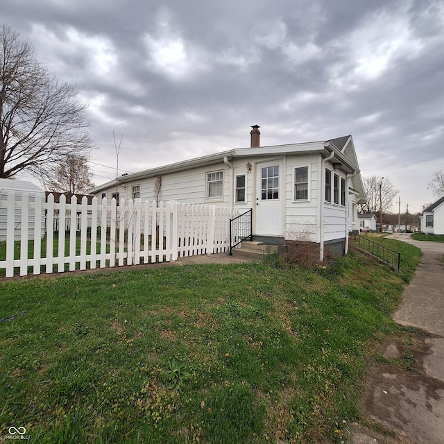view of front of home with a chimney, a front yard, and fence private yard