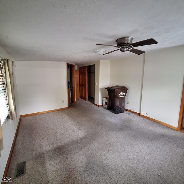 unfurnished living room with a wood stove, visible vents, ceiling fan, carpet flooring, and baseboards