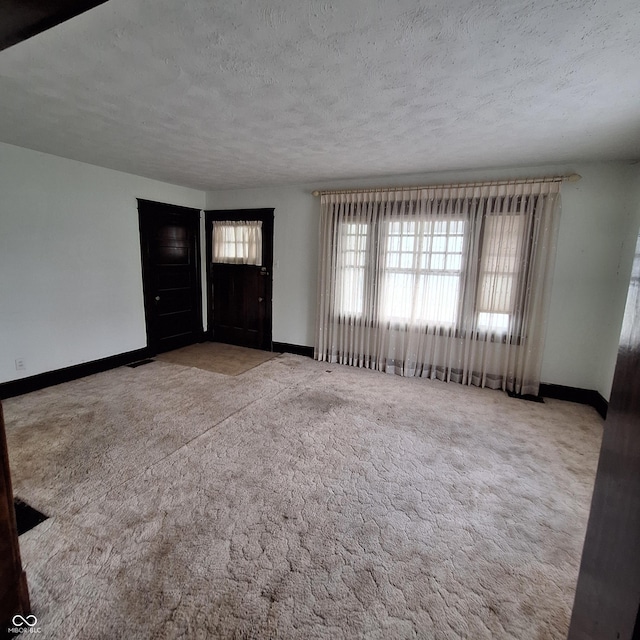 carpeted entrance foyer featuring a textured ceiling, visible vents, and baseboards