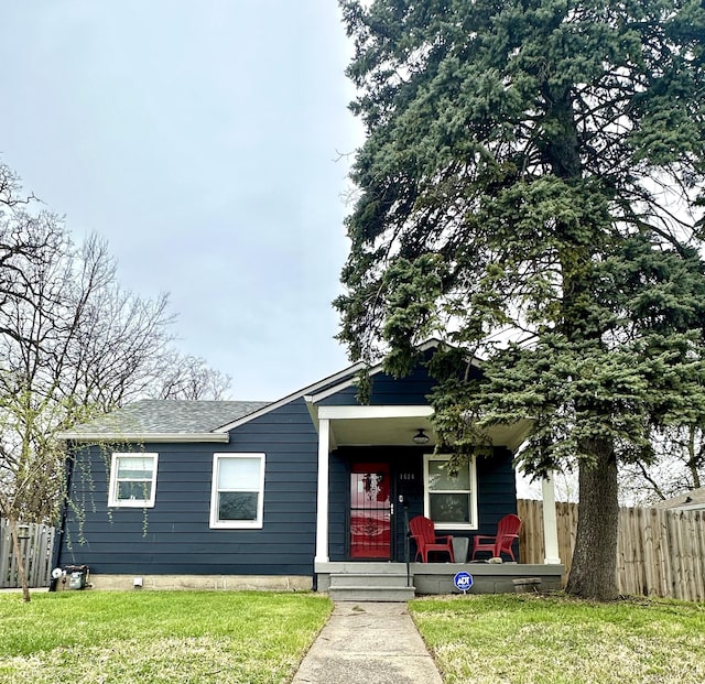 bungalow-style house with a shingled roof, a front yard, covered porch, and fence