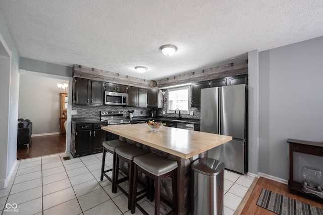 kitchen with a breakfast bar area, appliances with stainless steel finishes, a sink, butcher block counters, and light tile patterned flooring