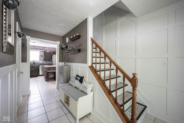 staircase featuring a textured ceiling, wainscoting, tile patterned flooring, and a decorative wall