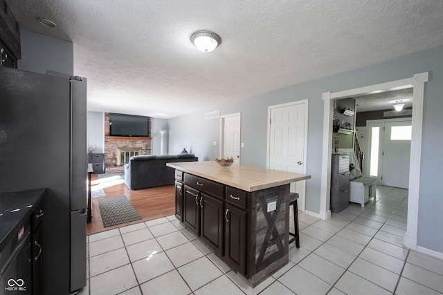 kitchen with visible vents, freestanding refrigerator, a brick fireplace, a breakfast bar area, and light tile patterned floors