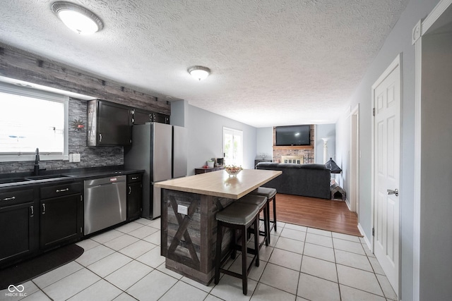 kitchen featuring a fireplace, a breakfast bar, a sink, light tile patterned floors, and stainless steel appliances