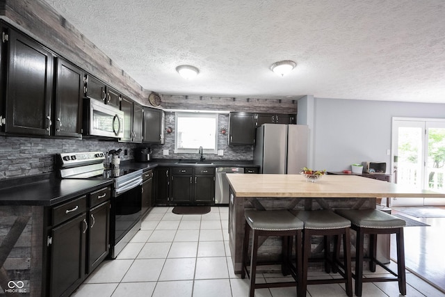 kitchen featuring a breakfast bar area, stainless steel appliances, dark cabinetry, and a sink