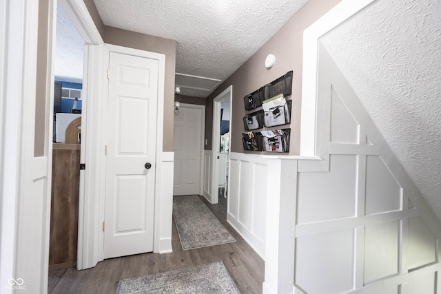 hall featuring a textured ceiling, wainscoting, wood finished floors, and attic access