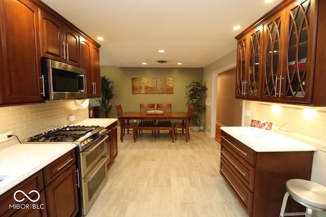 kitchen featuring recessed lighting, light countertops, glass insert cabinets, tasteful backsplash, and appliances with stainless steel finishes