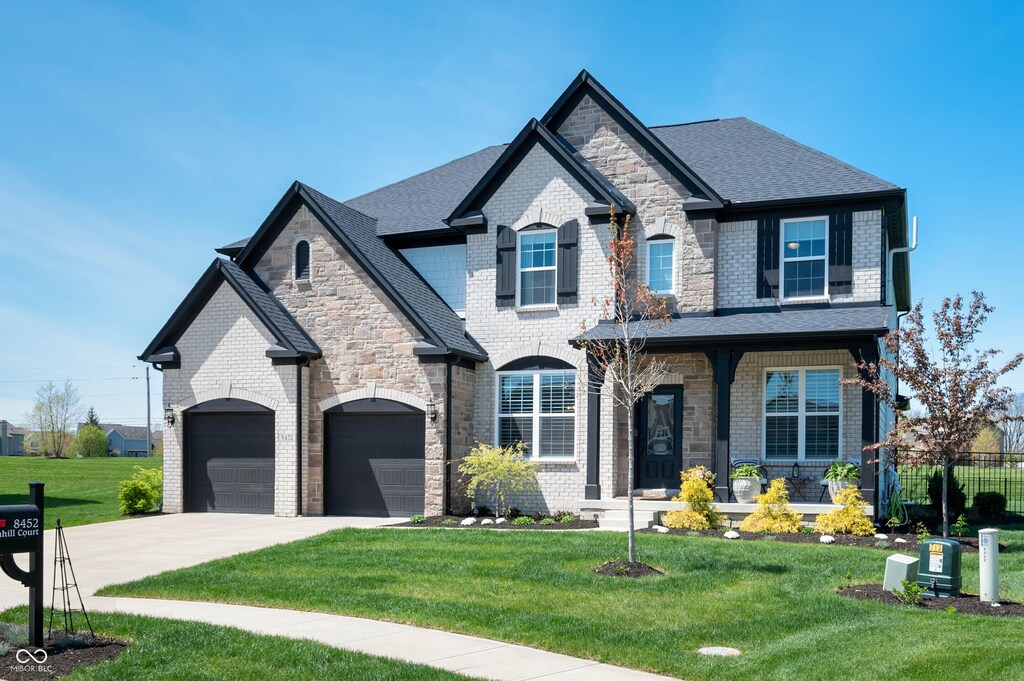 french country inspired facade with covered porch, a front yard, concrete driveway, and fence