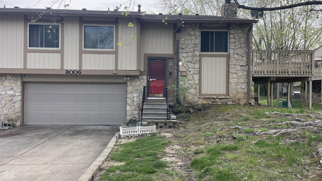 bi-level home with a chimney, a wooden deck, driveway, stone siding, and a garage