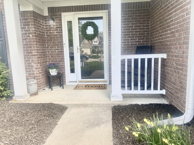view of exterior entry with brick siding and a porch