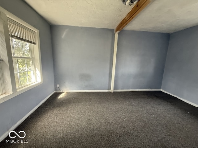 spare room featuring carpet floors, beam ceiling, and baseboards