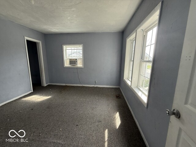 carpeted empty room featuring baseboards, a textured ceiling, and cooling unit