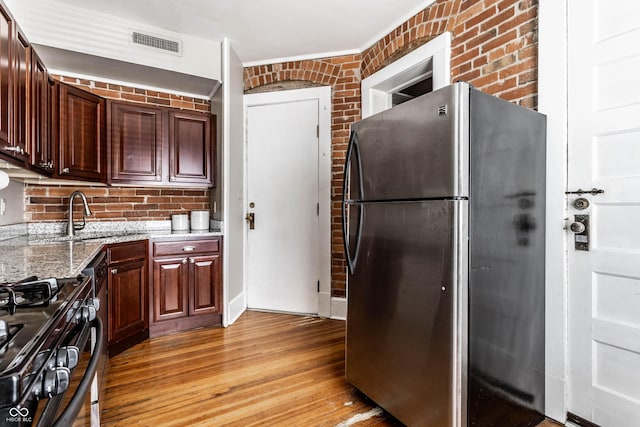 801 N Pennsylvania St Apt D, Indianapolis, IN 46204 - kitchen with freestanding refrigerator, black gas range oven, a sink, light wood-style floors, and brick wall
