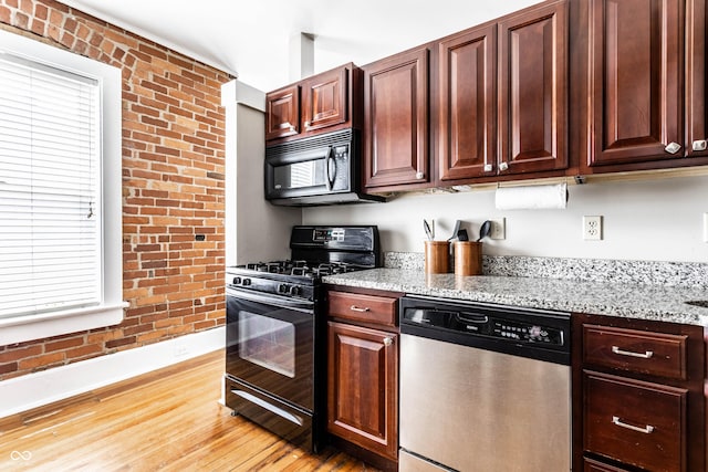 801 N Pennsylvania St Apt D, Indianapolis, IN 46204 - kitchen with black appliances, baseboards, brick wall, light stone counters, and light wood-style flooring