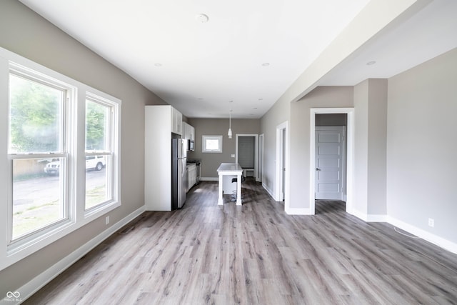 unfurnished living room with visible vents, light wood finished floors, and baseboards