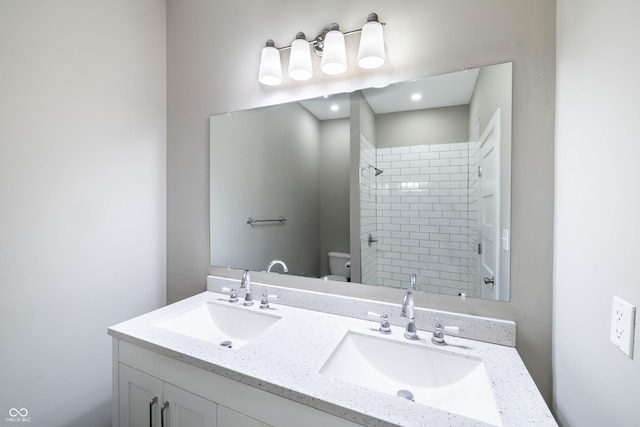 bathroom with a tile shower, double vanity, toilet, and a sink