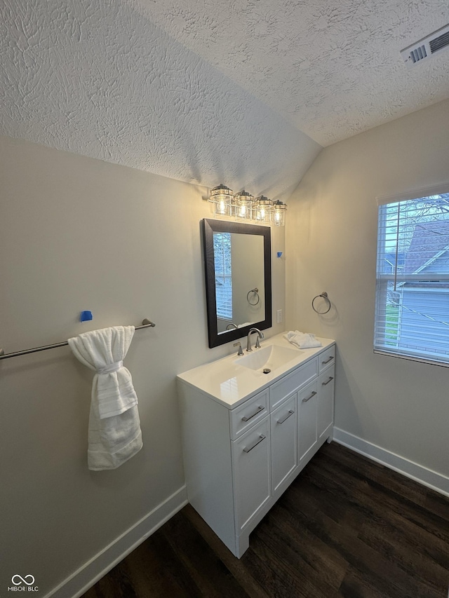 bathroom featuring a textured ceiling, vaulted ceiling, baseboards, visible vents, and wood finished floors