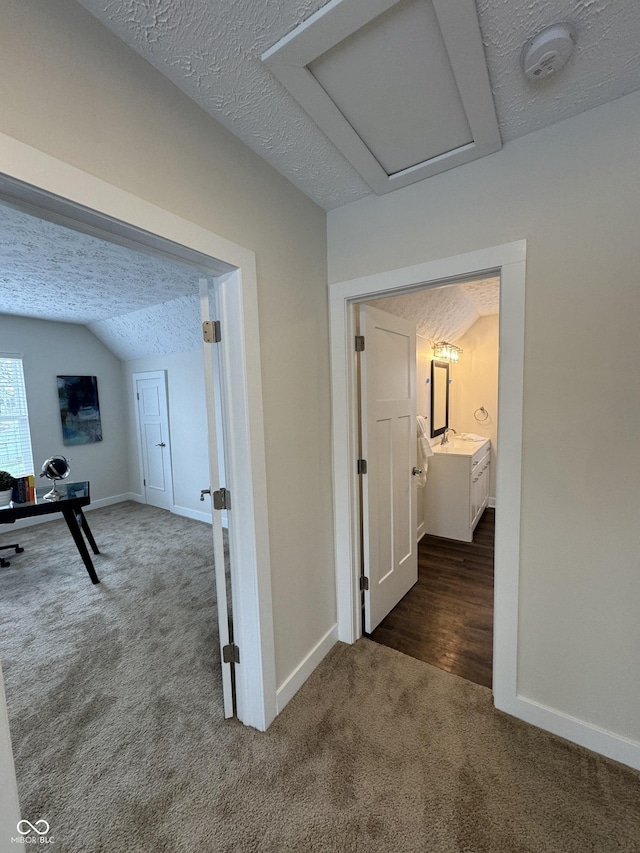 hallway featuring dark carpet, baseboards, and a textured ceiling