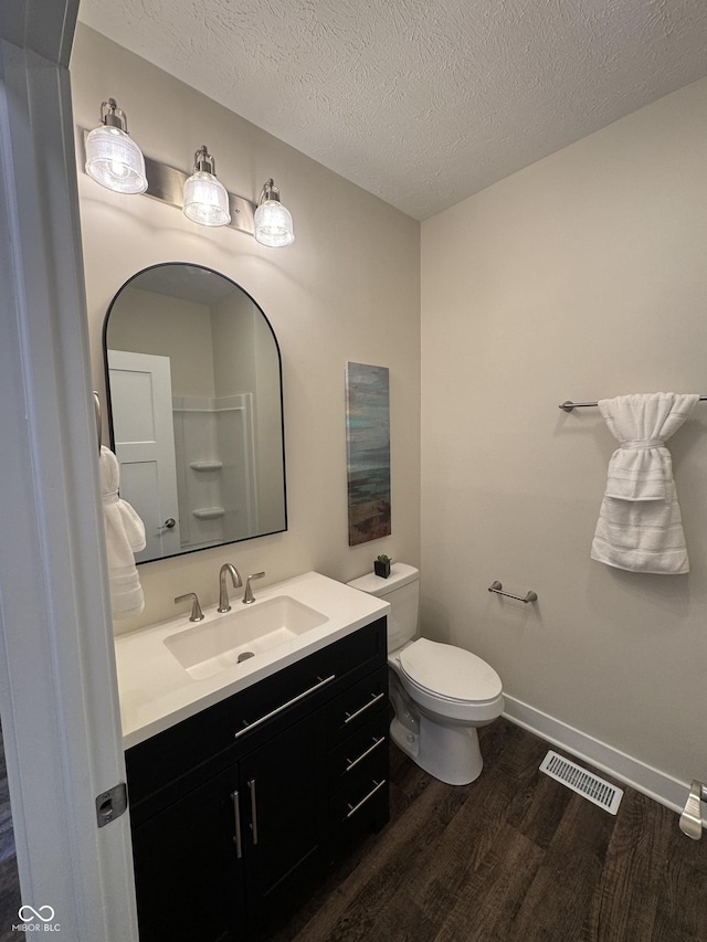 bathroom with wood finished floors, visible vents, toilet, vanity, and a textured ceiling