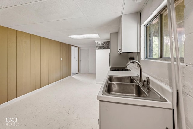 kitchen with light countertops, a drop ceiling, wood walls, and a sink
