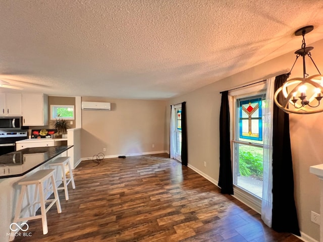 unfurnished dining area with dark wood-style flooring, a textured ceiling, a chandelier, and a wall mounted air conditioner