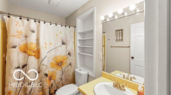 bathroom featuring curtained shower, visible vents, toilet, vanity, and a textured ceiling