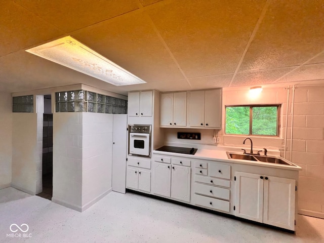 kitchen featuring a sink, oven, black electric cooktop, white cabinetry, and concrete block wall