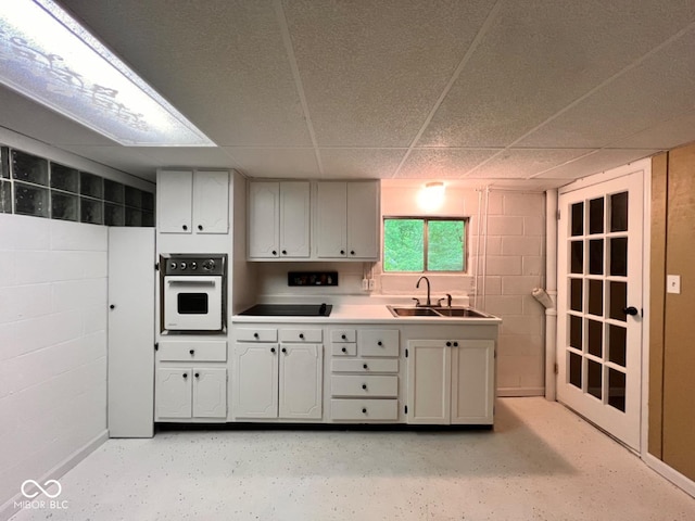 kitchen featuring concrete block wall, black electric cooktop, a sink, a drop ceiling, and white oven