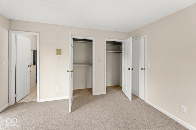 unfurnished bedroom featuring two closets, baseboards, and carpet flooring