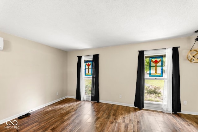 unfurnished room featuring plenty of natural light, baseboards, wood finished floors, and a textured ceiling