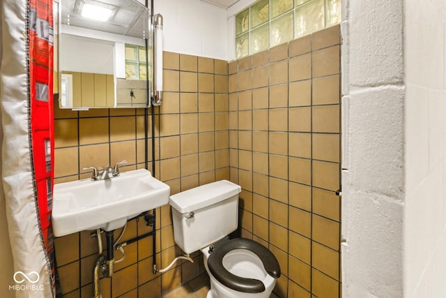 bathroom with toilet, a sink, and tile walls