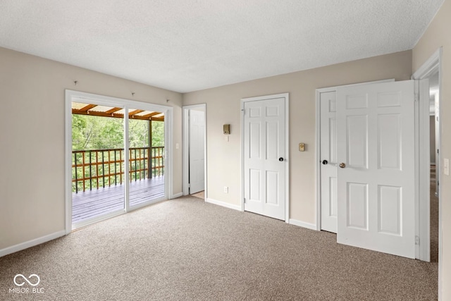 unfurnished bedroom with a textured ceiling, two closets, carpet floors, baseboards, and access to exterior