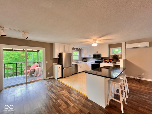 kitchen featuring white cabinets, a wall unit AC, baseboards, a textured ceiling, and appliances with stainless steel finishes