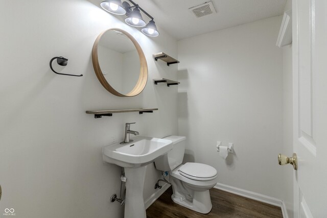 half bathroom featuring baseboards, toilet, wood finished floors, and visible vents