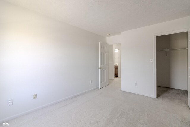 unfurnished bedroom featuring light colored carpet, baseboards, a walk in closet, and a closet