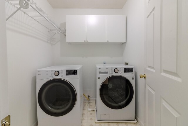 clothes washing area with cabinet space, washer and clothes dryer, and light floors
