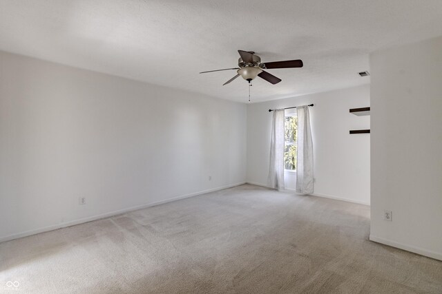 empty room with ceiling fan, light colored carpet, baseboards, and visible vents